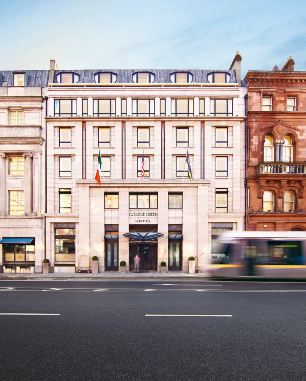Elegant facade of College Green Hotel Dublin with a bus passing.