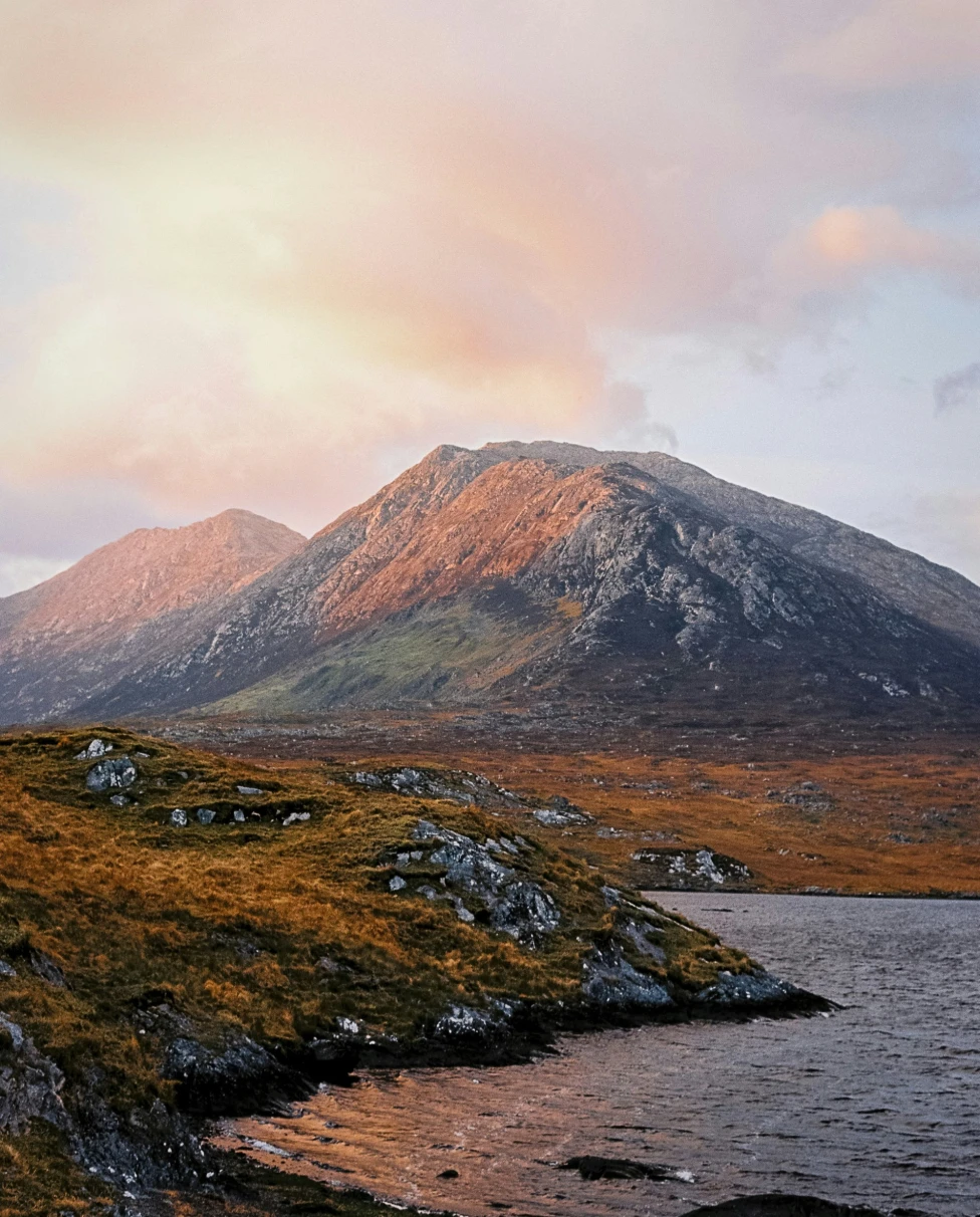 Lake with mountains at the back with pink and yellow clouds.