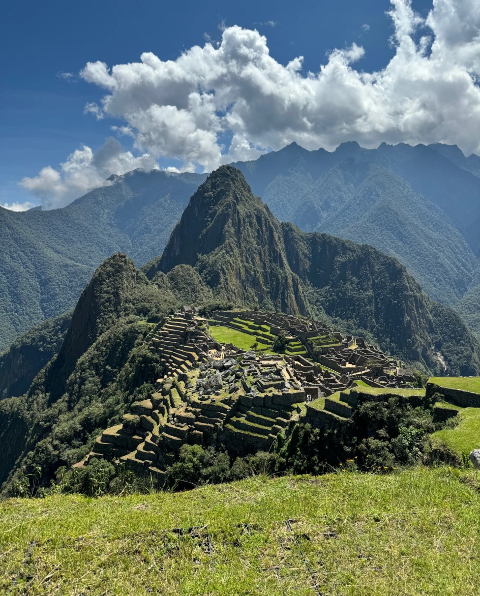 A distant view of Machu Picchu on a sunny day, with mountain ranges and peaks in the distance.