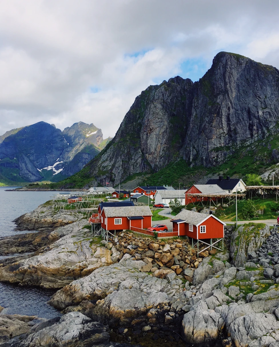 Red houses next to mountain and body of water with cloudy skies during daytime