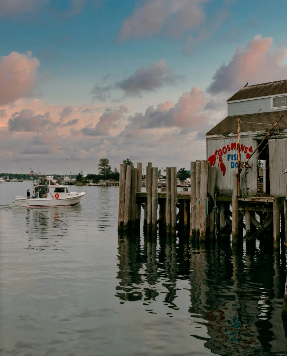 The image shows a pier with a white building with a red painted sign saying 'Gosmans', at sunset with pink fluffy clouds.