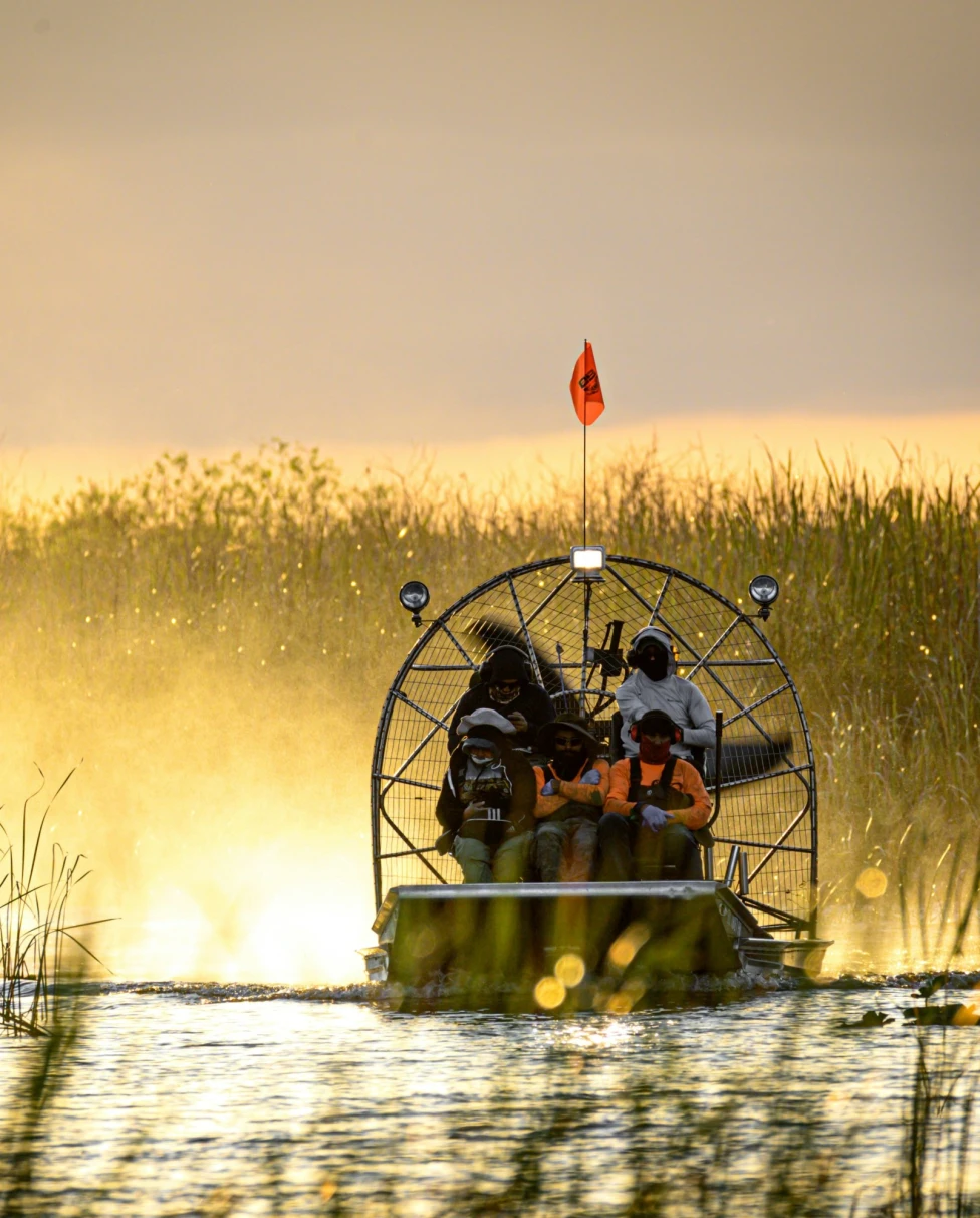 People in a fan boat travel in a swamp.