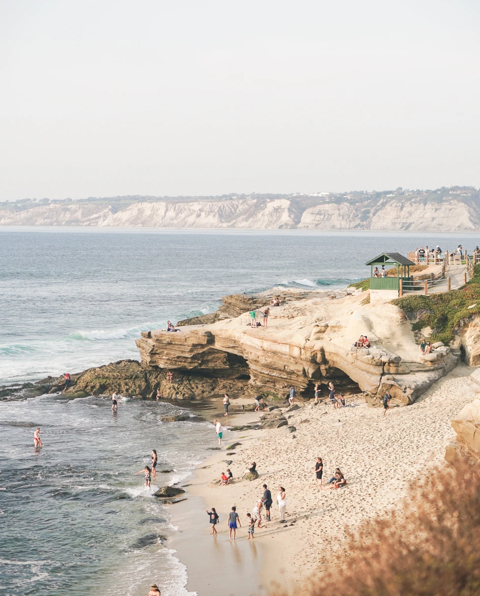 People stand on the sand and in the water on La Jolla Cove in San Diego