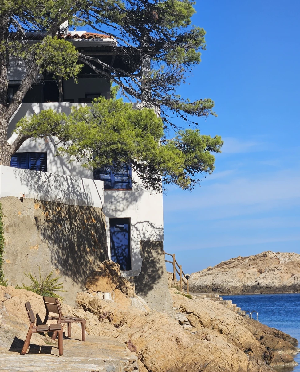 A white and blue house built into the rocky terrain on the coast of Begur, on a sunny day in Spain.