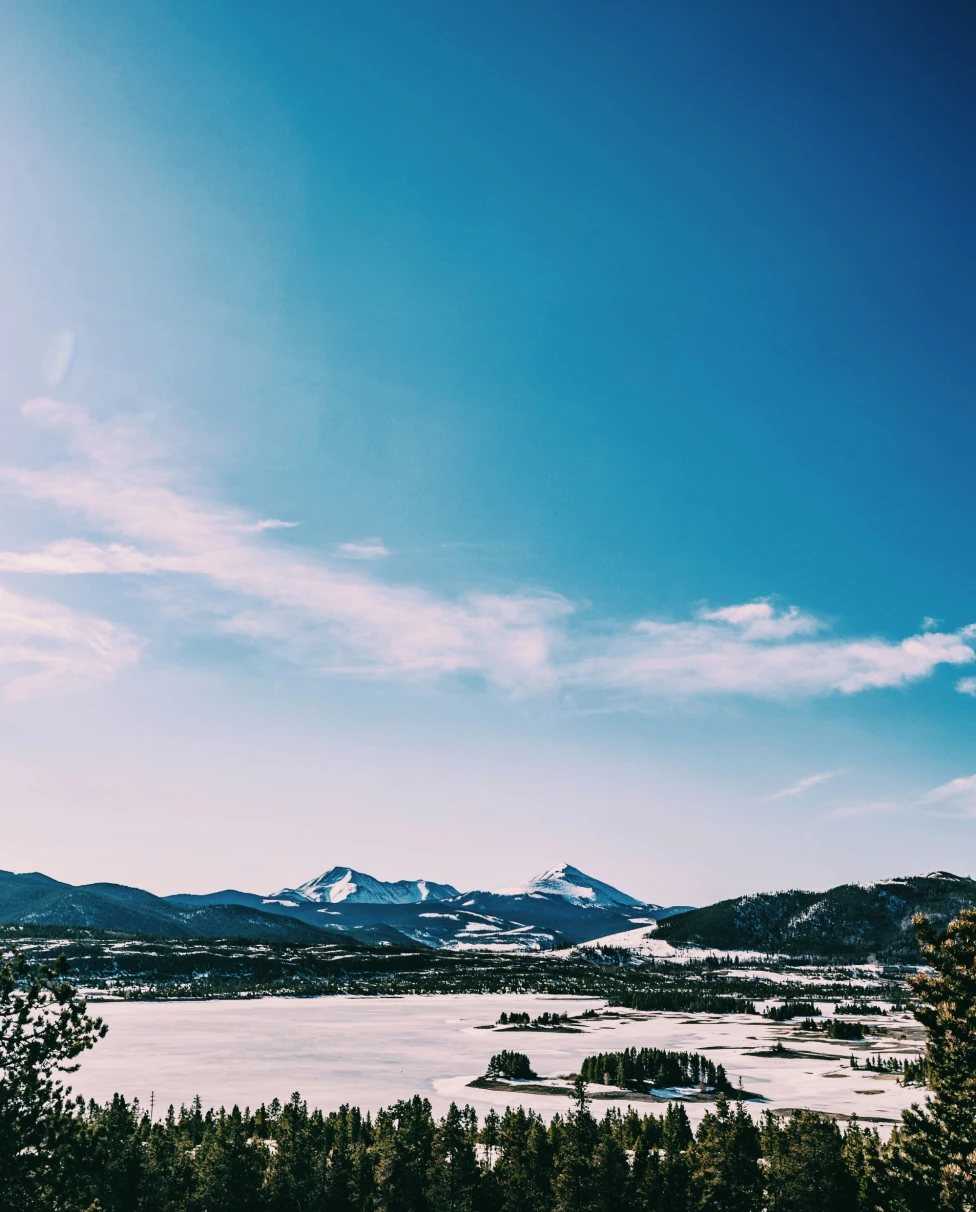 A serene snowy landscape with distant mountains under a clear blue sky, bathed in bright sunlight, in Aspen in winter.
