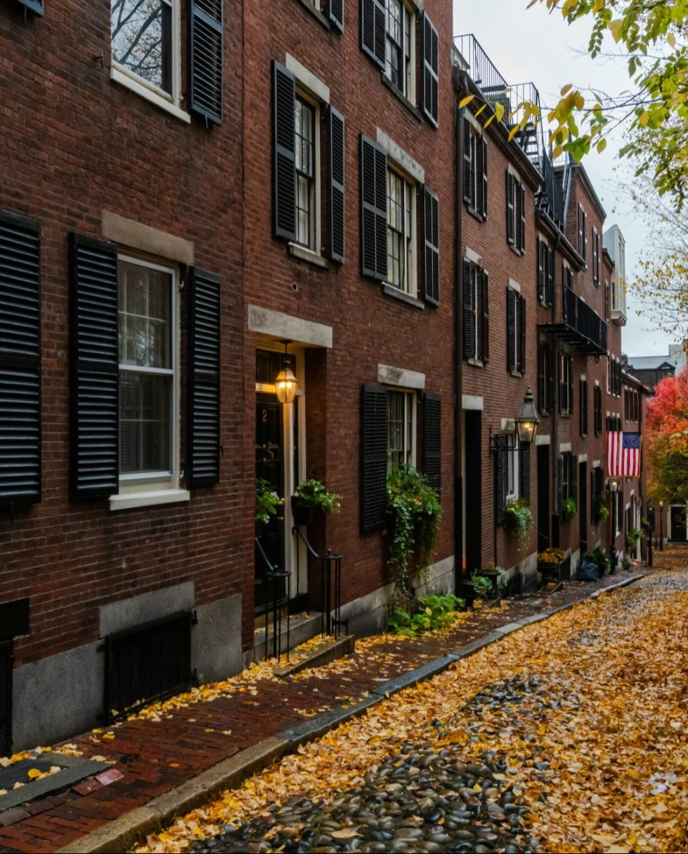 Pathway in front of red brick building with fall leaves.