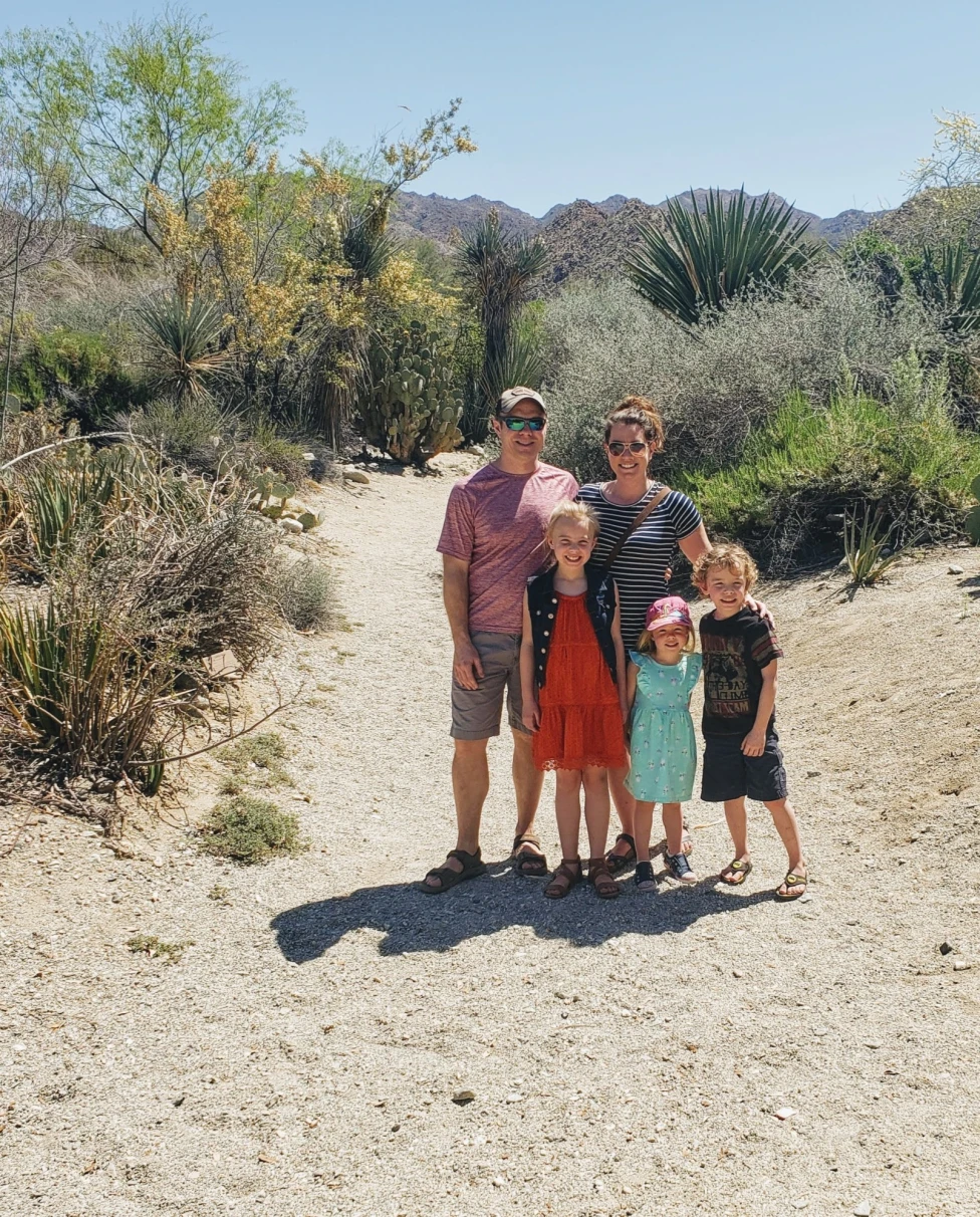 A family posing in a desert landscape on a bright sunny day surrounded by cactus, shrubs and other desert plants.