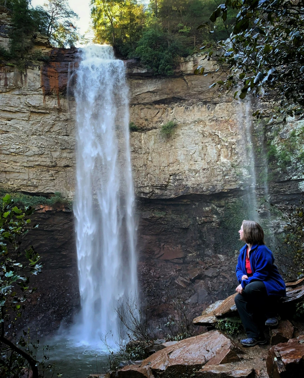 A person sitting on a rock next to a waterfall during the daytime.