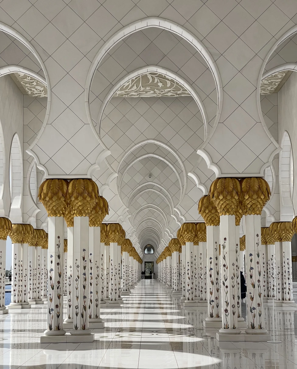 A white and gold mosque with several rows of arches and pillars in the UAE.