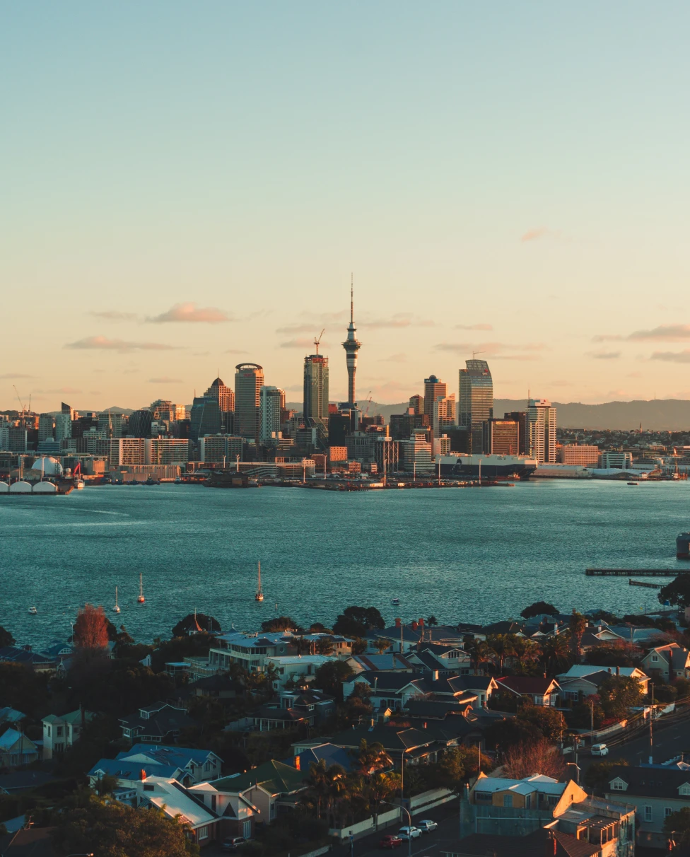 A city view of Auckland, New Zealand at sunset overlooking a blue lake.
