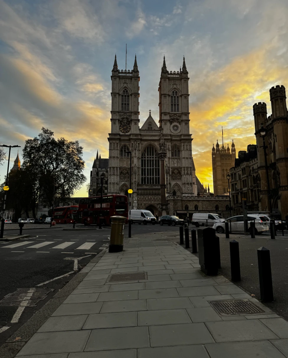 A London street displaying a prominent, stone, church building against a multi-colored sky.