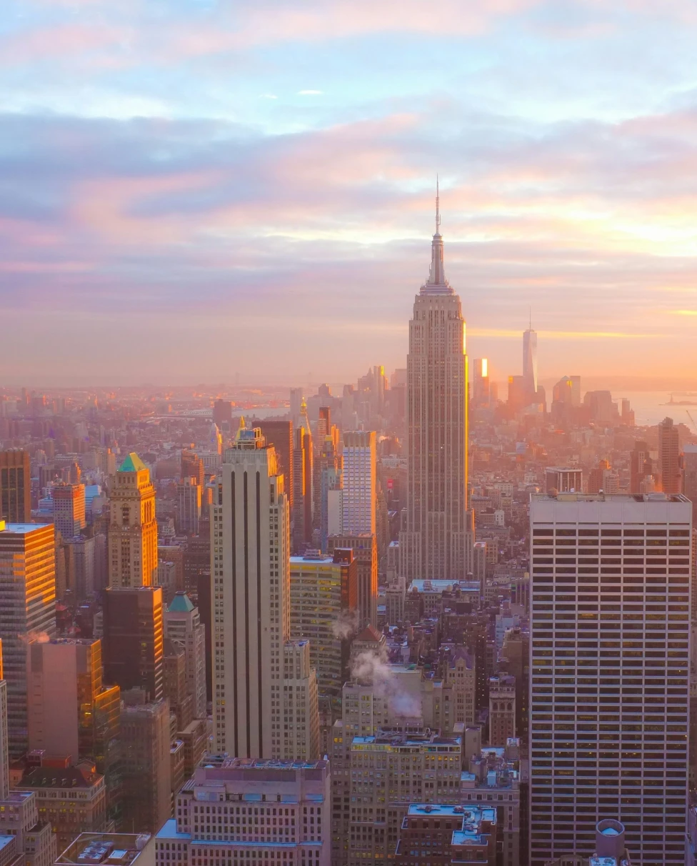 A view of Midtown Manhattan's skyline, the Empire State Building, Hudson River and Lady Liberty underneath a colorful sunset.
