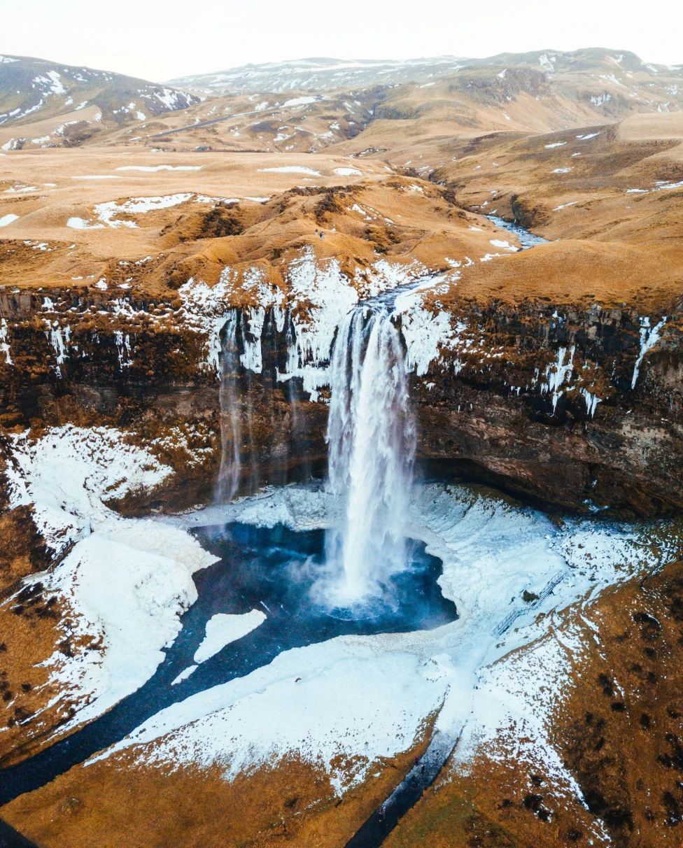 An aerial photo of a frozen waterfall near the mountains.