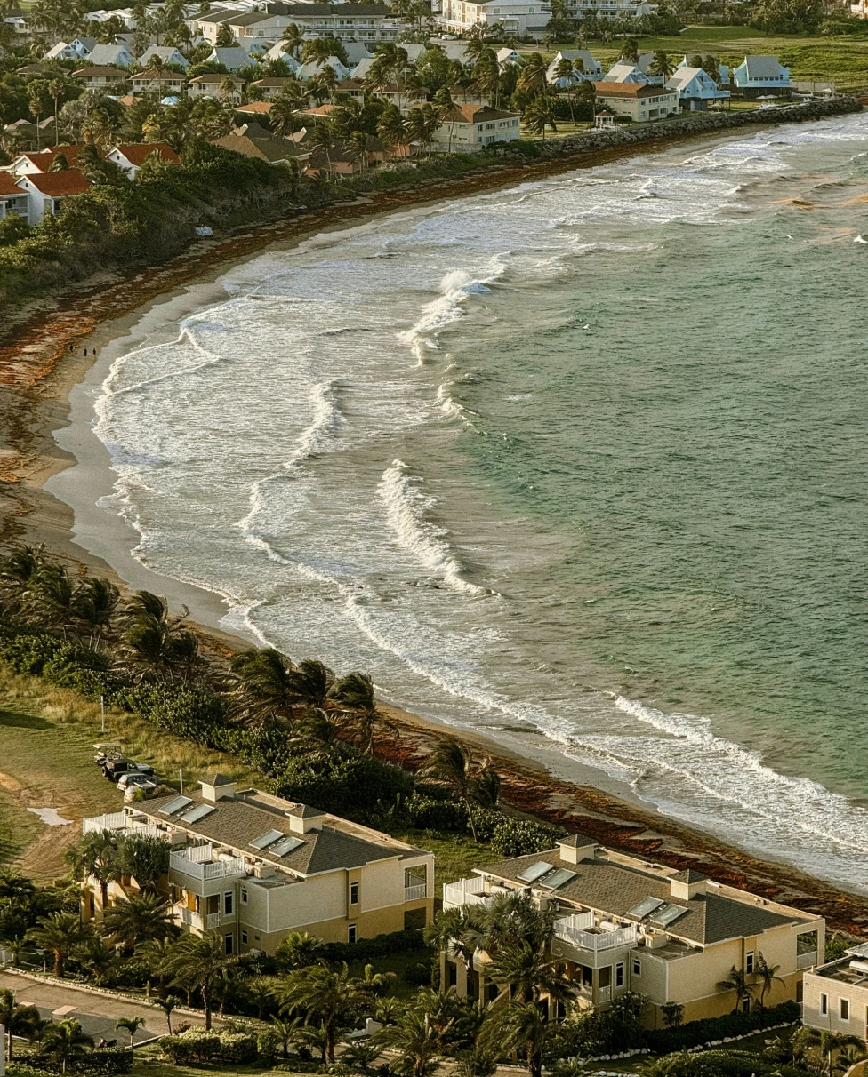 The image depicts a serene coastal scene with houses along the shoreline and waves gently approaching the beach.