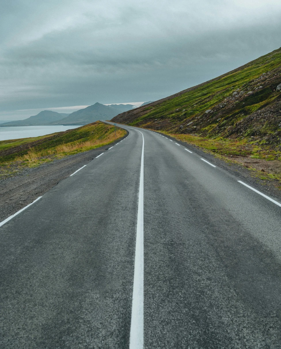 The image depicts a road leading into the distance, flanked by mountains and a cloudy sky, evoking a sense of journey and exploration.