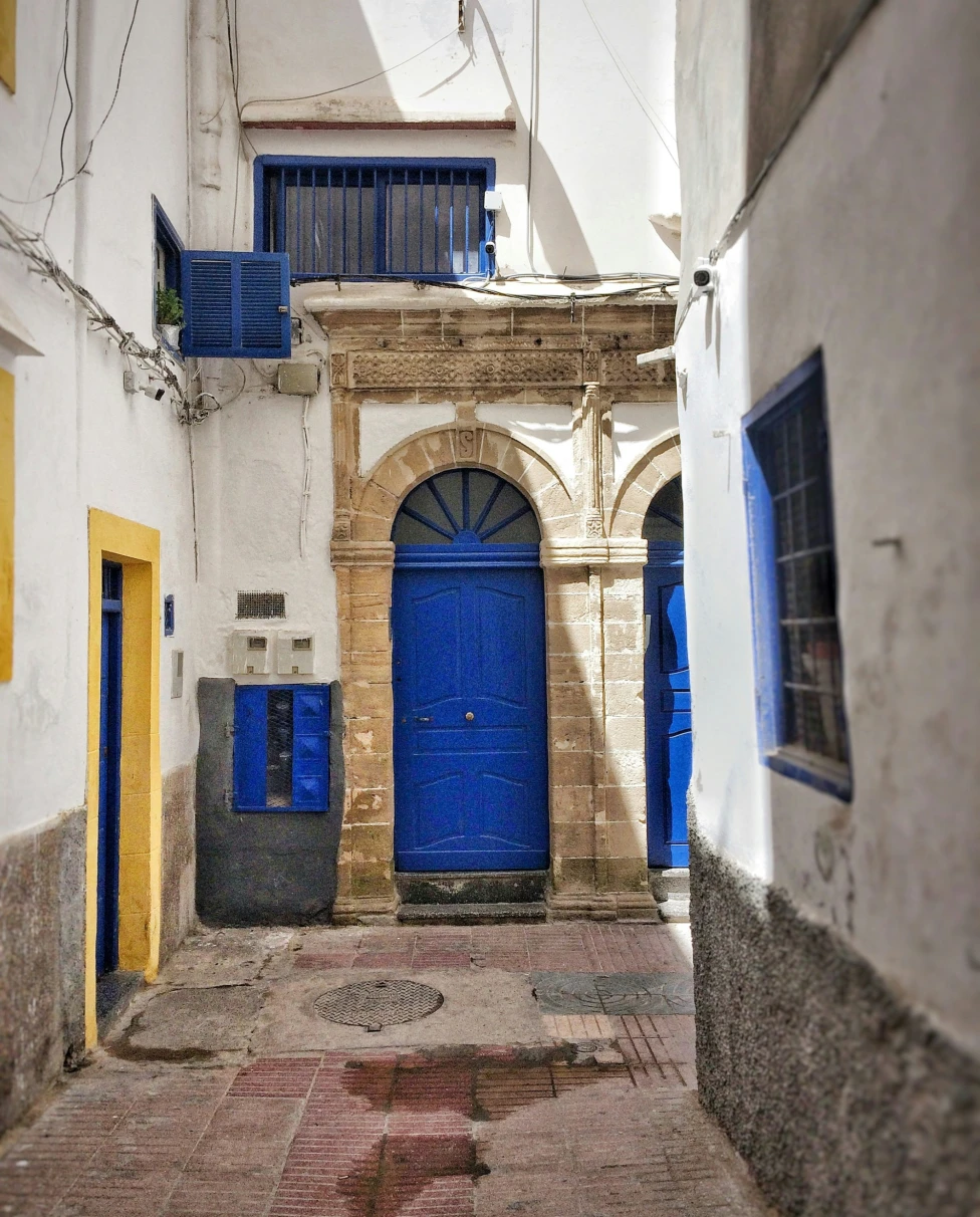 A quaint white-walled stone alleyway with a striking blue door and windows.