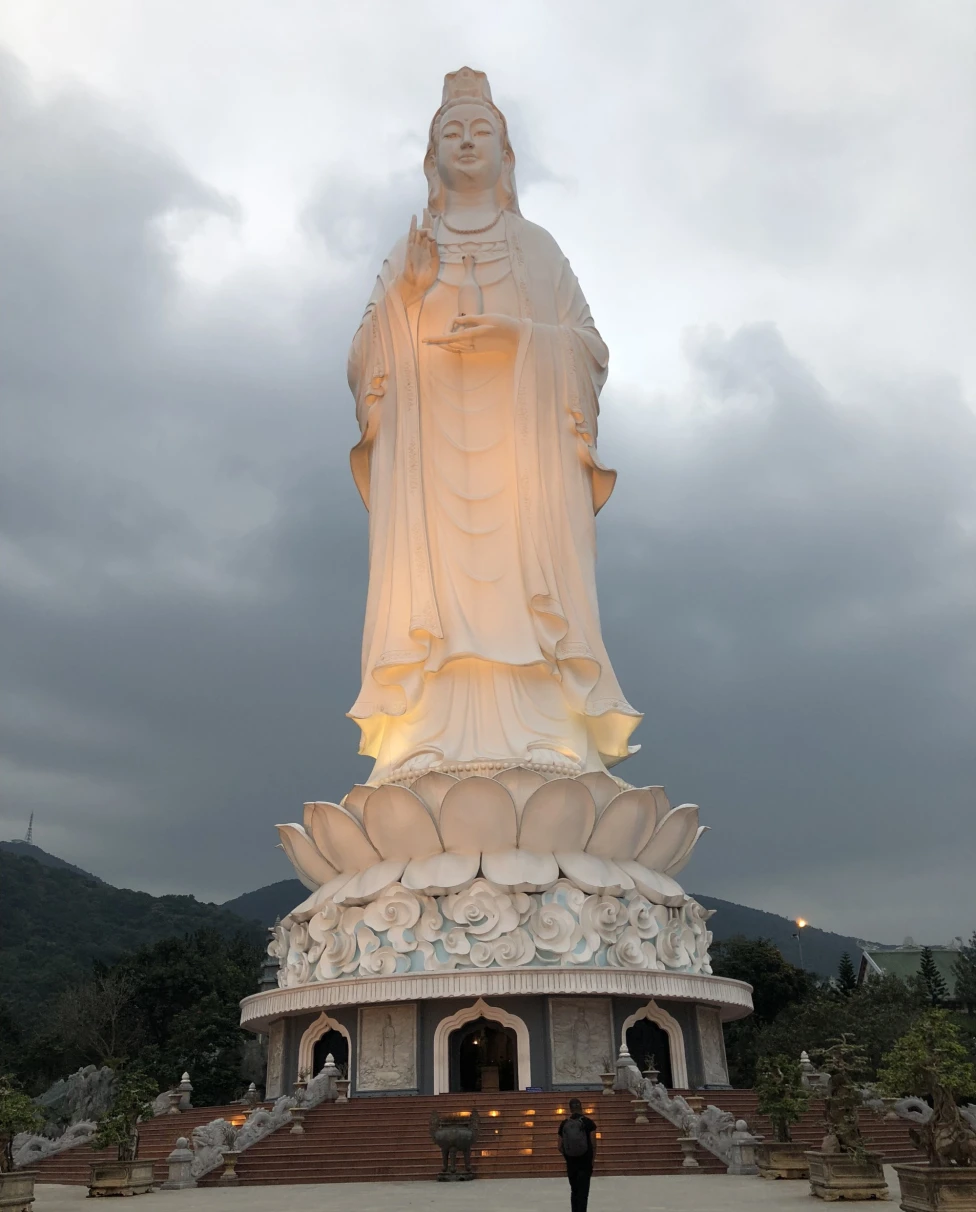 A low-angled shot of a Lady Buddha statue made out of a white stone and lit up at daytime.