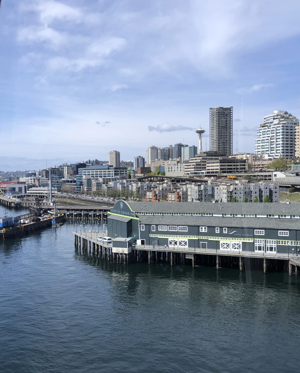 An aerial view of Seattle's skyline with the Seattle Aquarium in the forefront on a sunny day.