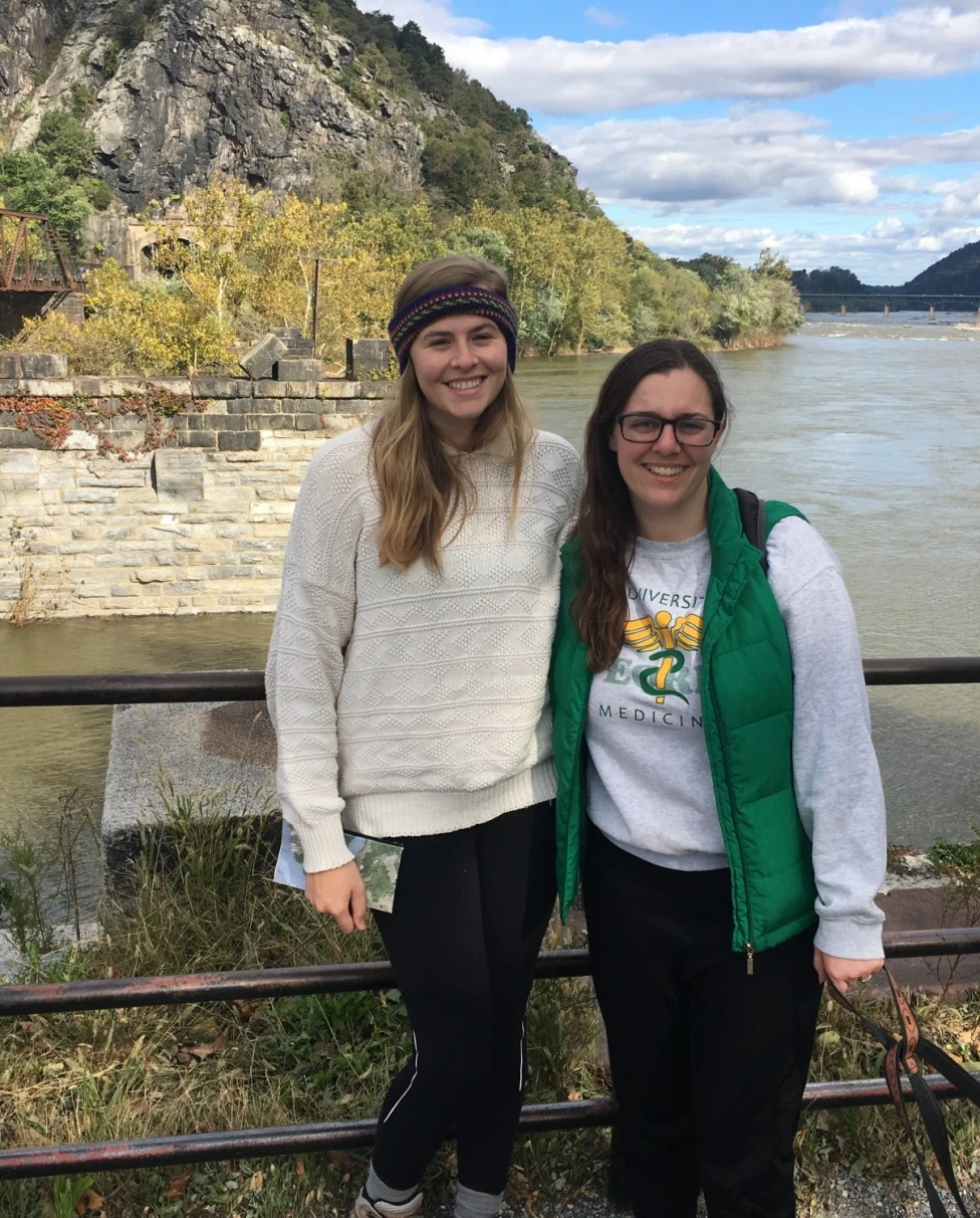 Two women in front of a lake surrounded by rocky hills.
