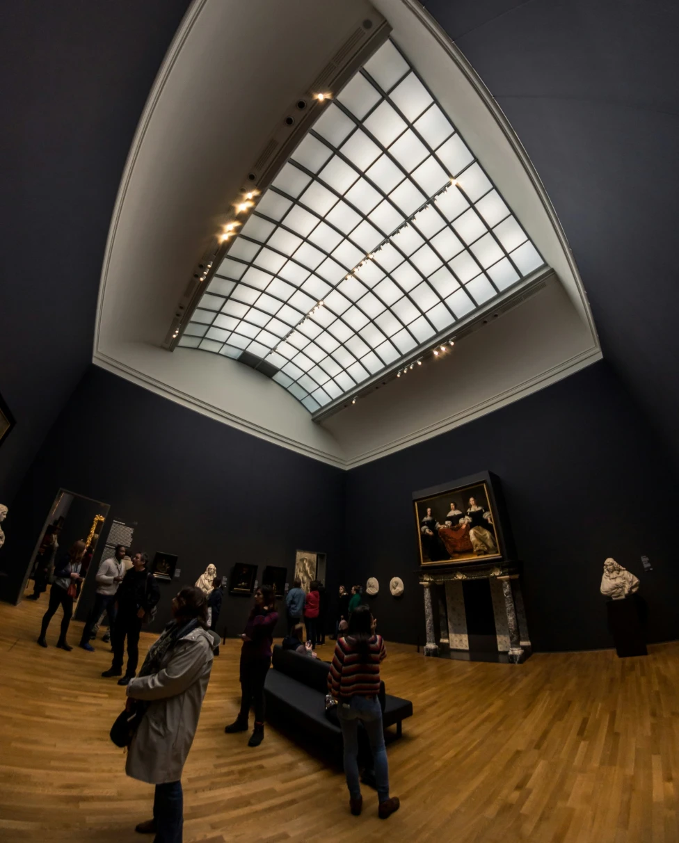 Rijks Museum features a modern skylight filtering light into the high-ceilinged gallery space as guests peruse art.