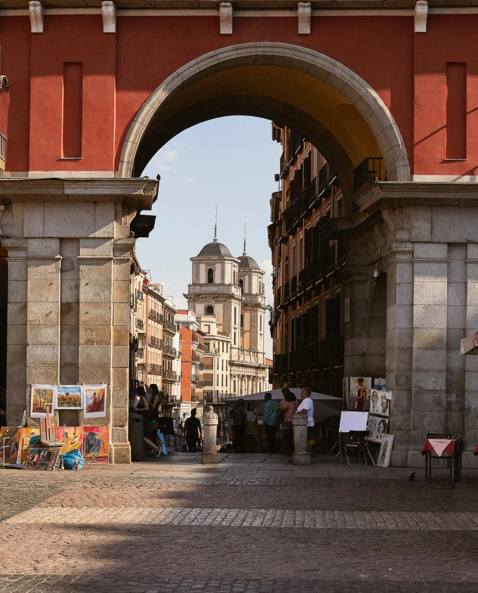 a large archway leads into a narrow city street with vendors and artists