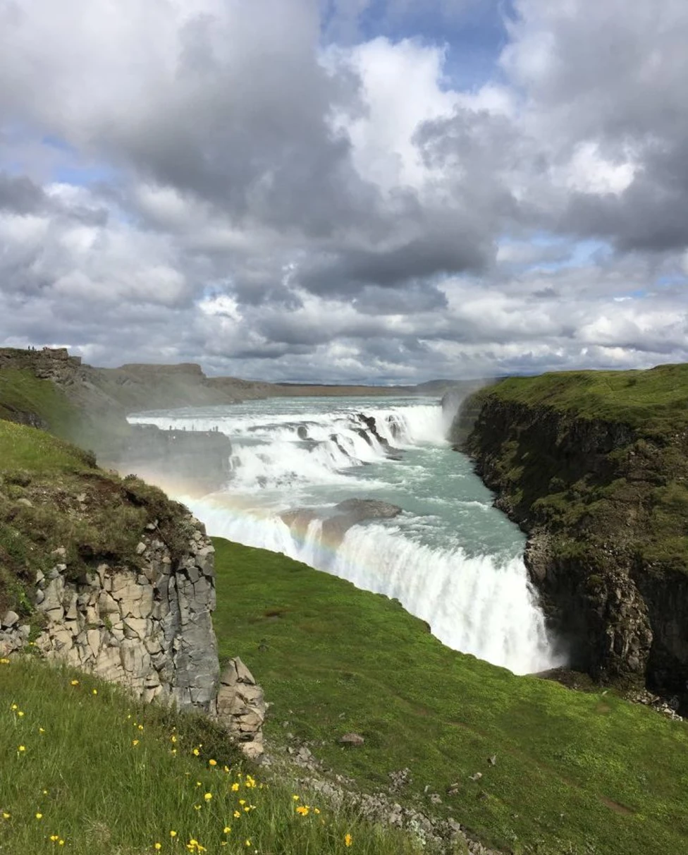 A vast waterfall next to grass-covered hills during the daytime