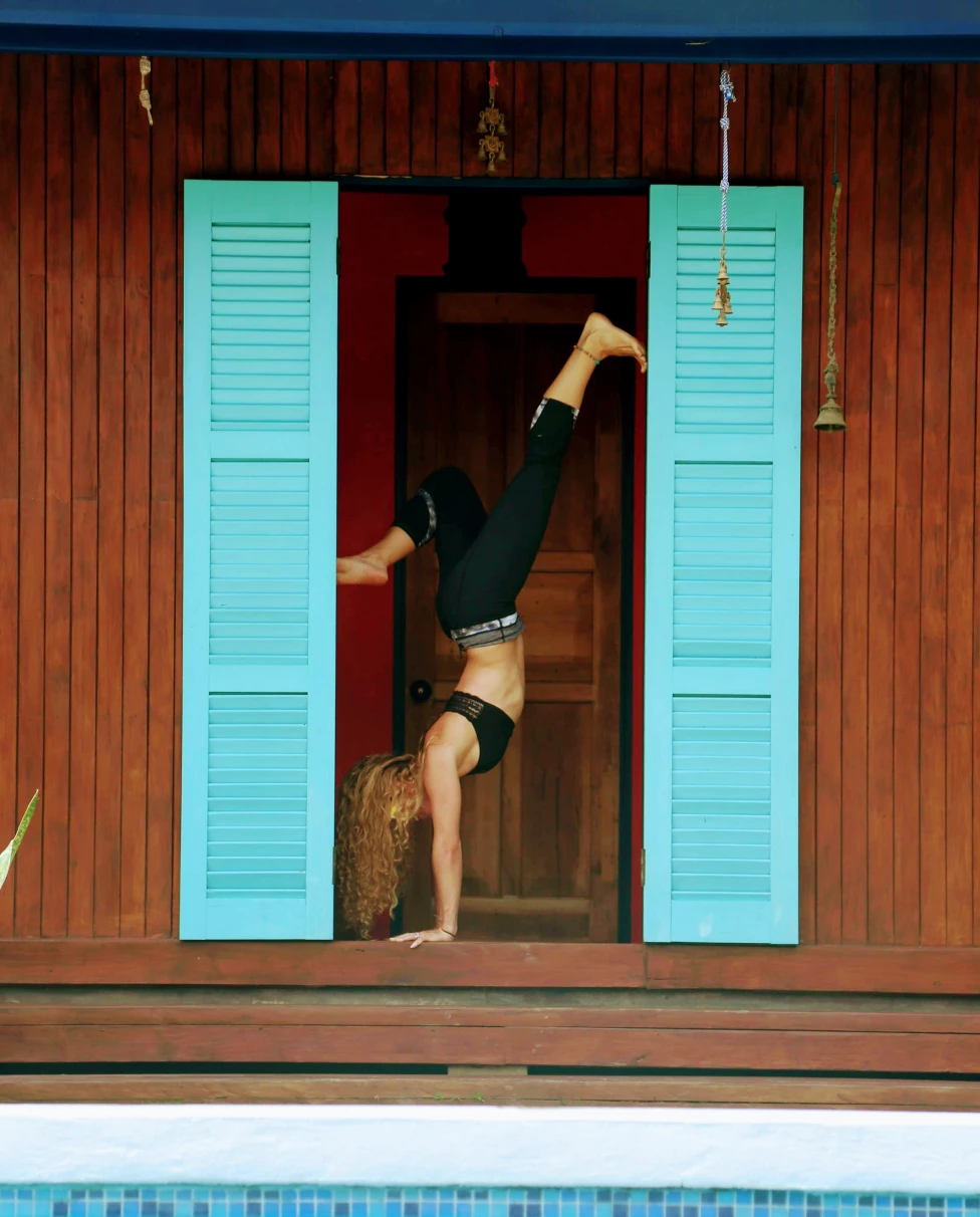 A yogi doing a headstand next to a blue door in Costa Rica.