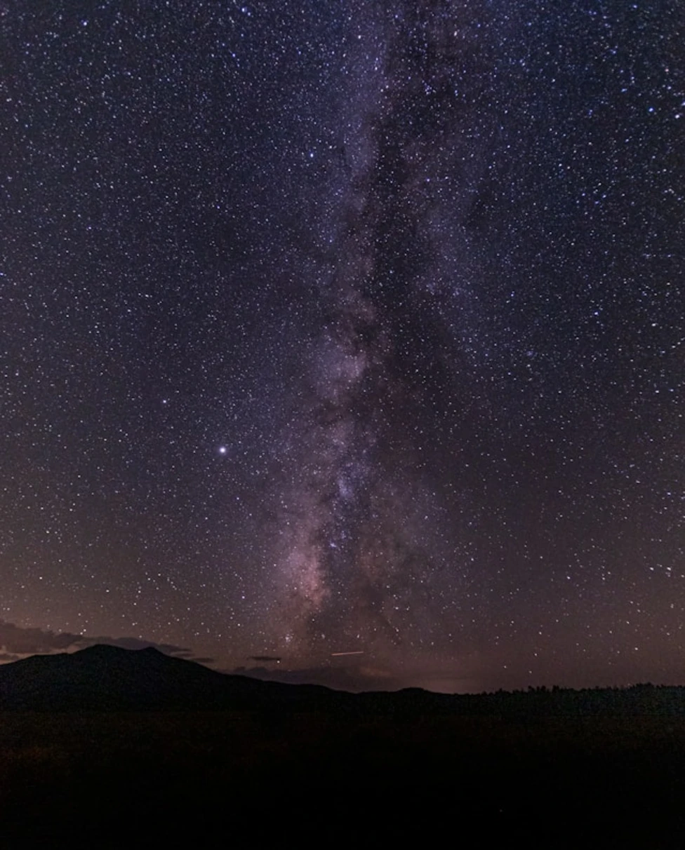 A view of a beautiful starry constellation at nighttime above a dark mountain top.