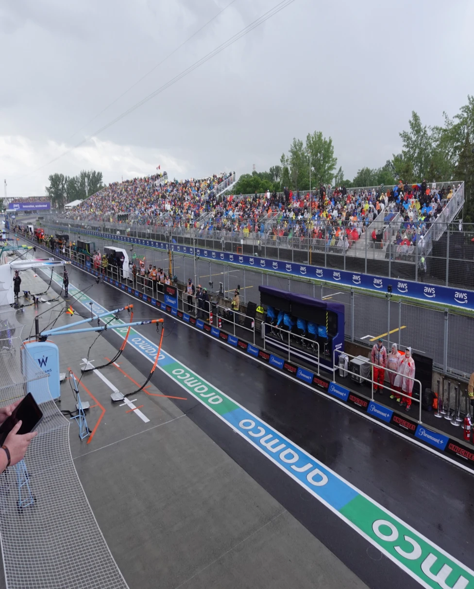 A bustling grandstand overlooks the adrenaline-fueled precision of a motorsport race, under a sky hinting at the unpredictability of nature.
