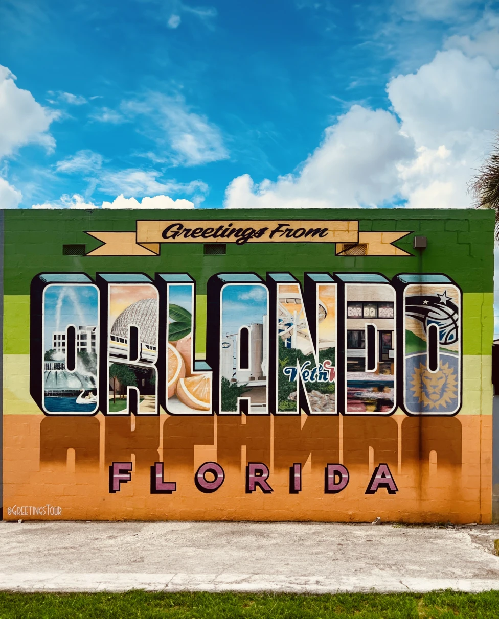 Signage saying "Greetings From Orlando" against a clear blue sky dotted with wispy clouds.