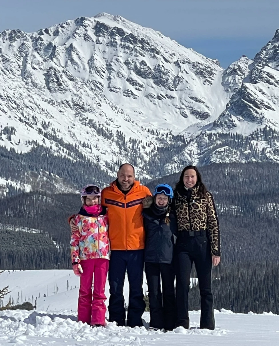 A picture of a family posing in front of a snowy mountain during the daytime.