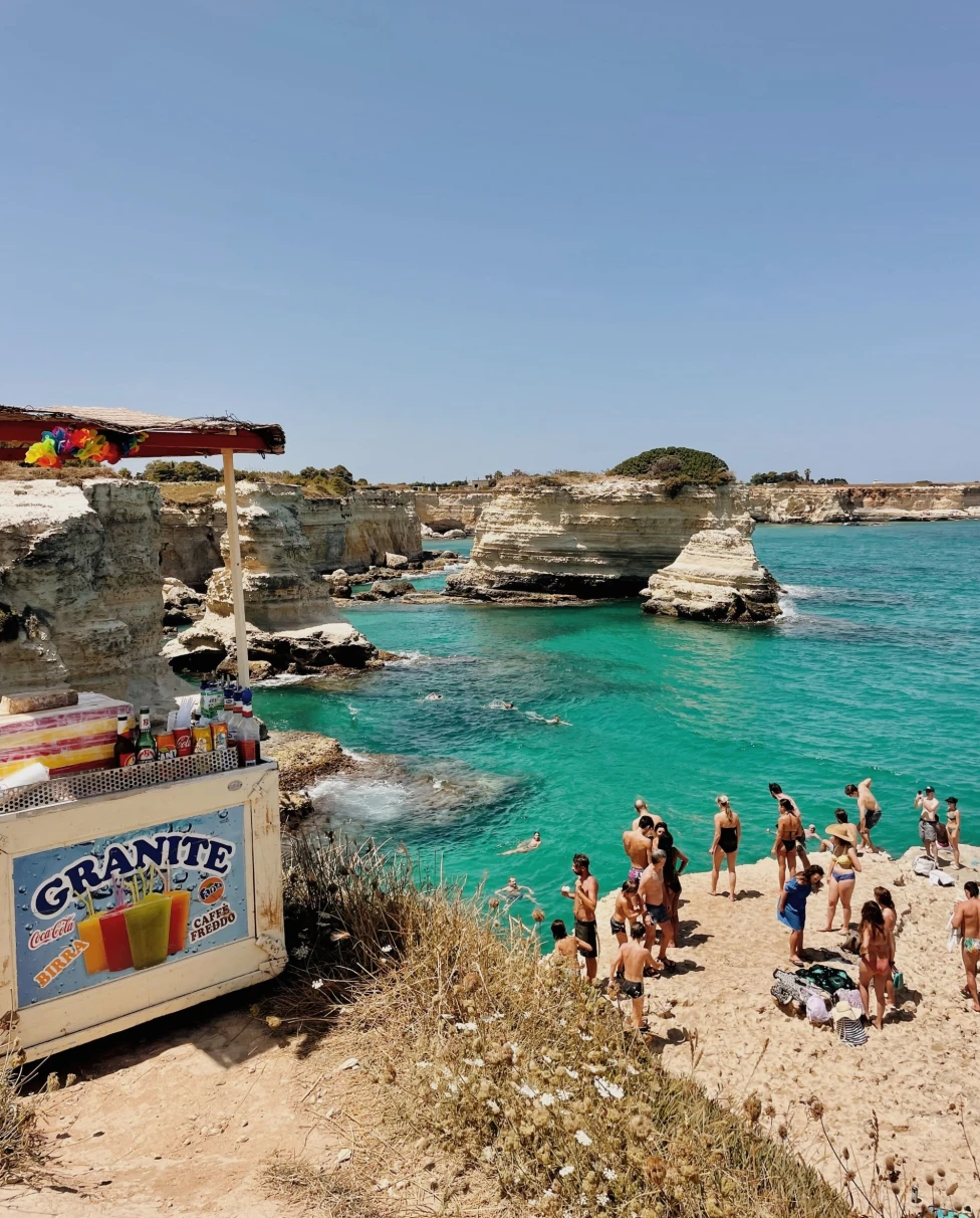 An aerial view of the beach with people standing on shore during daytime.