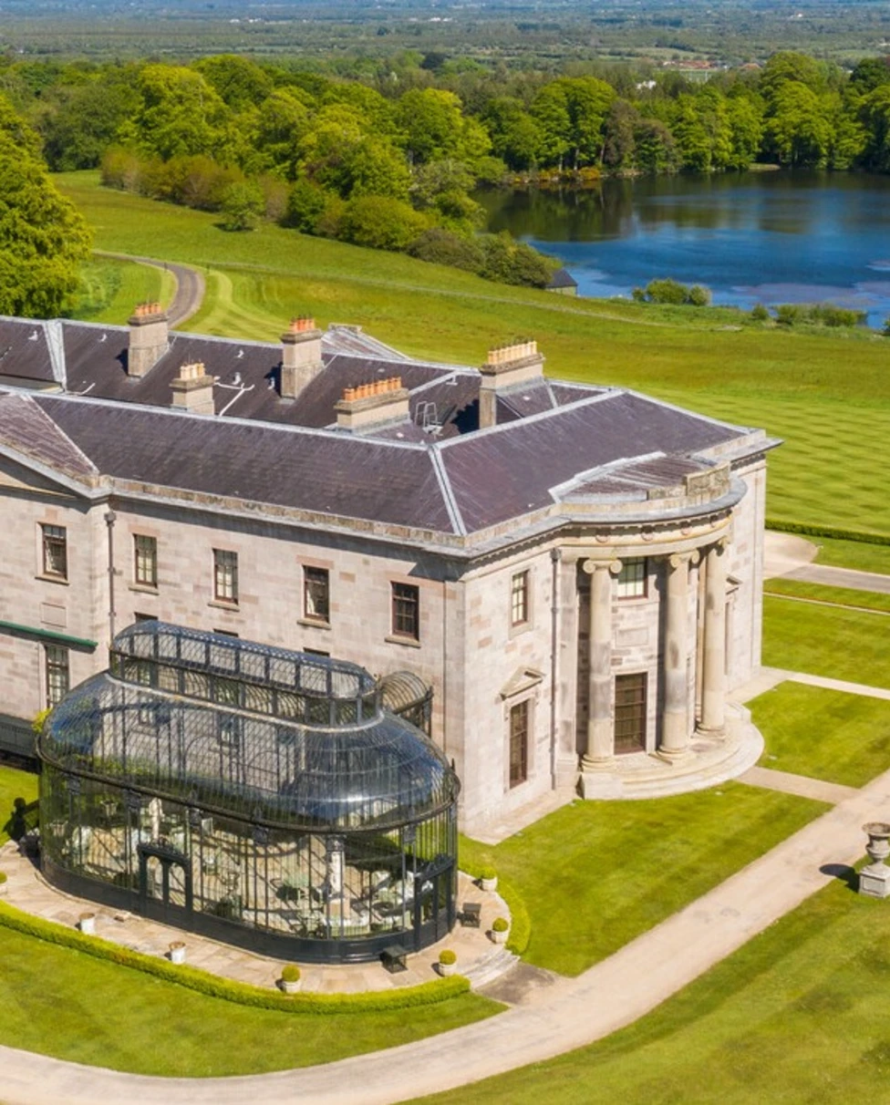 A large manor on a green lawn with a lake in the distance