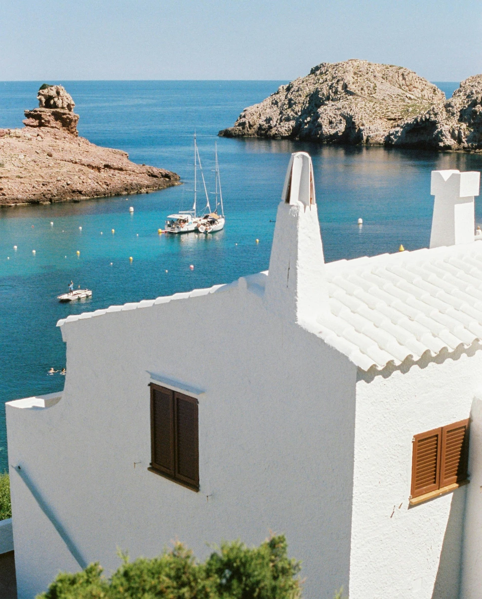 An aerial view of a Mediterranean coastal town, with a view of buildings, mountains, and the azure sea.