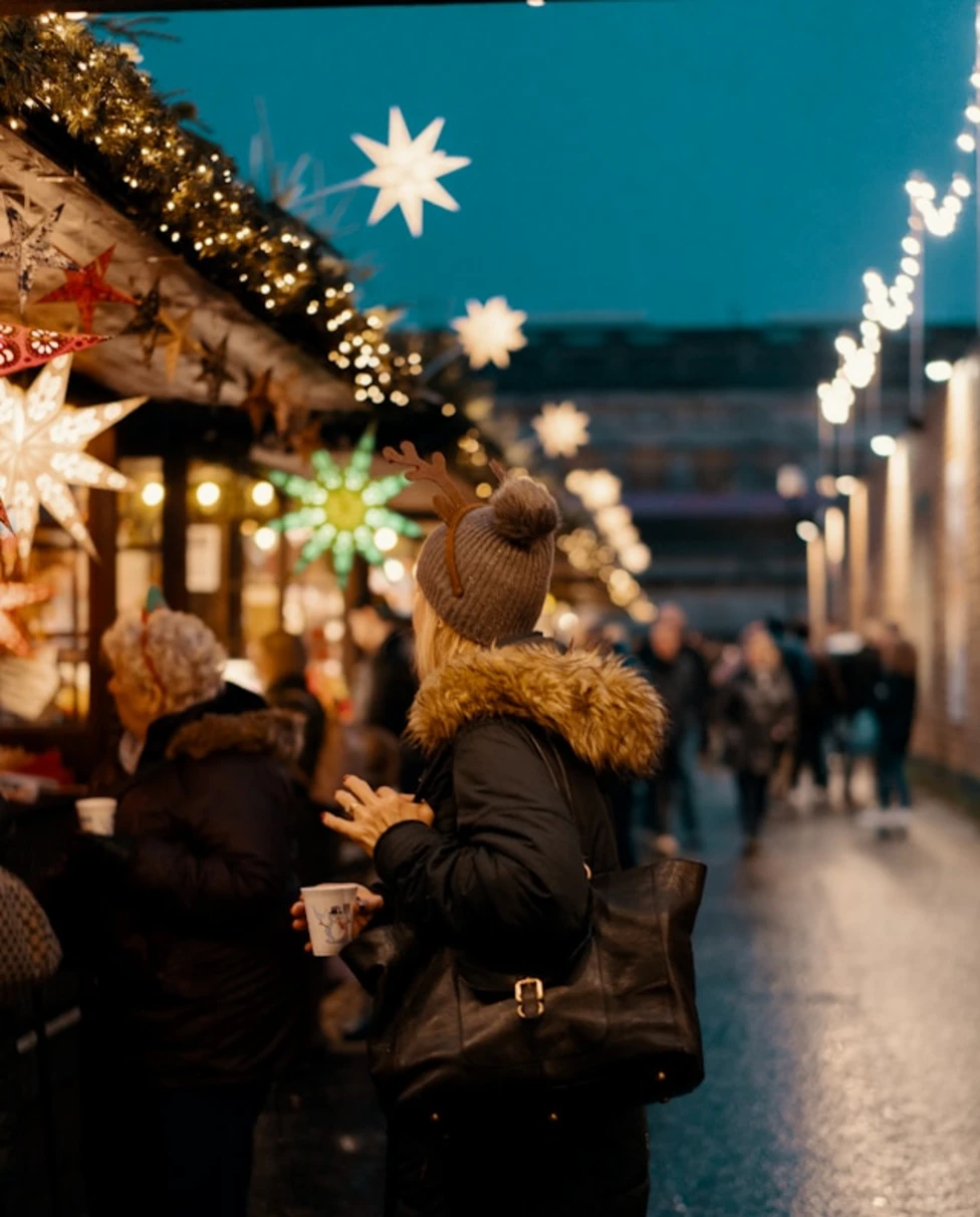 A view of people at the Chistmas Market in Ediburgh at night with christmas light decorations and market stands