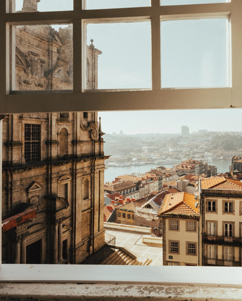 Window view of Porto featuring a street, church, ocean and local houses.