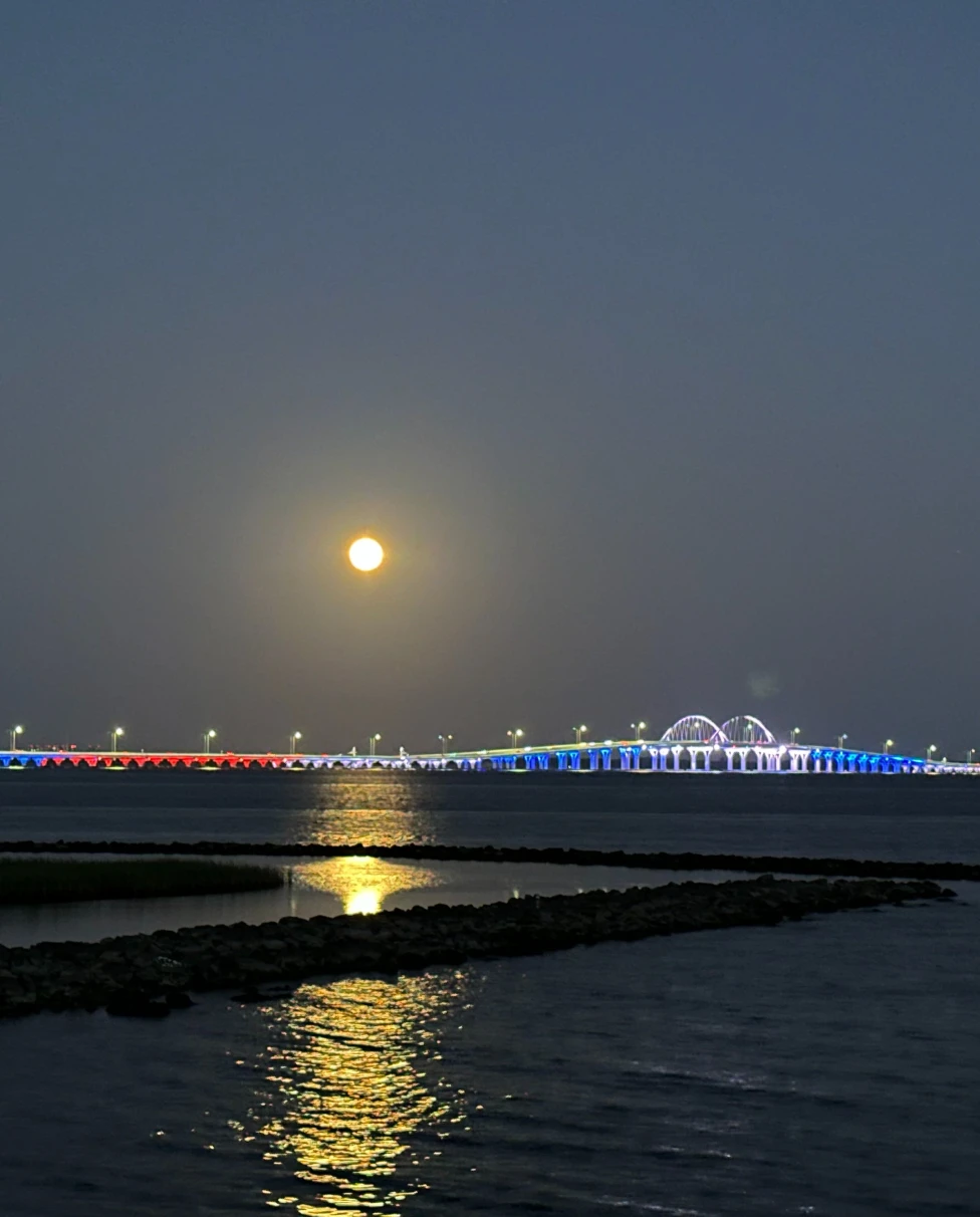 Pensacola's Three Mile Bridge lit up in red white and blue with a full moon overhead.