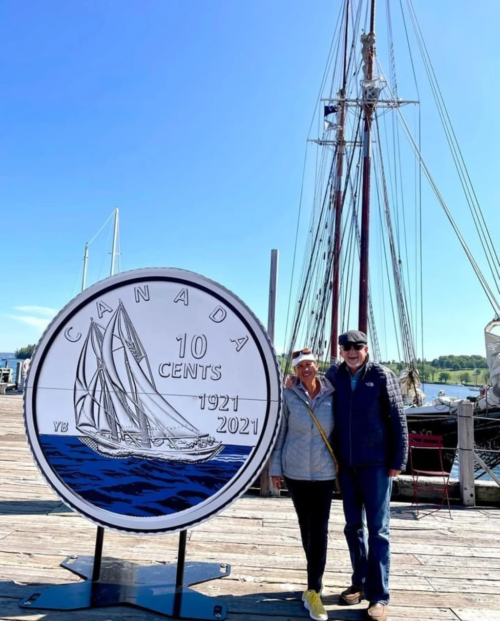 Diana and a man standing next to a giant Canadian dime in front of boats in the harbor