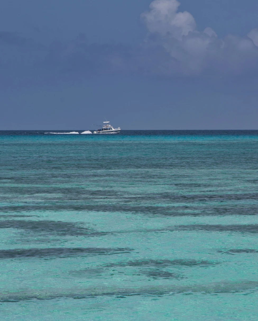Different shades of turquoise ocean with blue sky and a boat in the far distance.