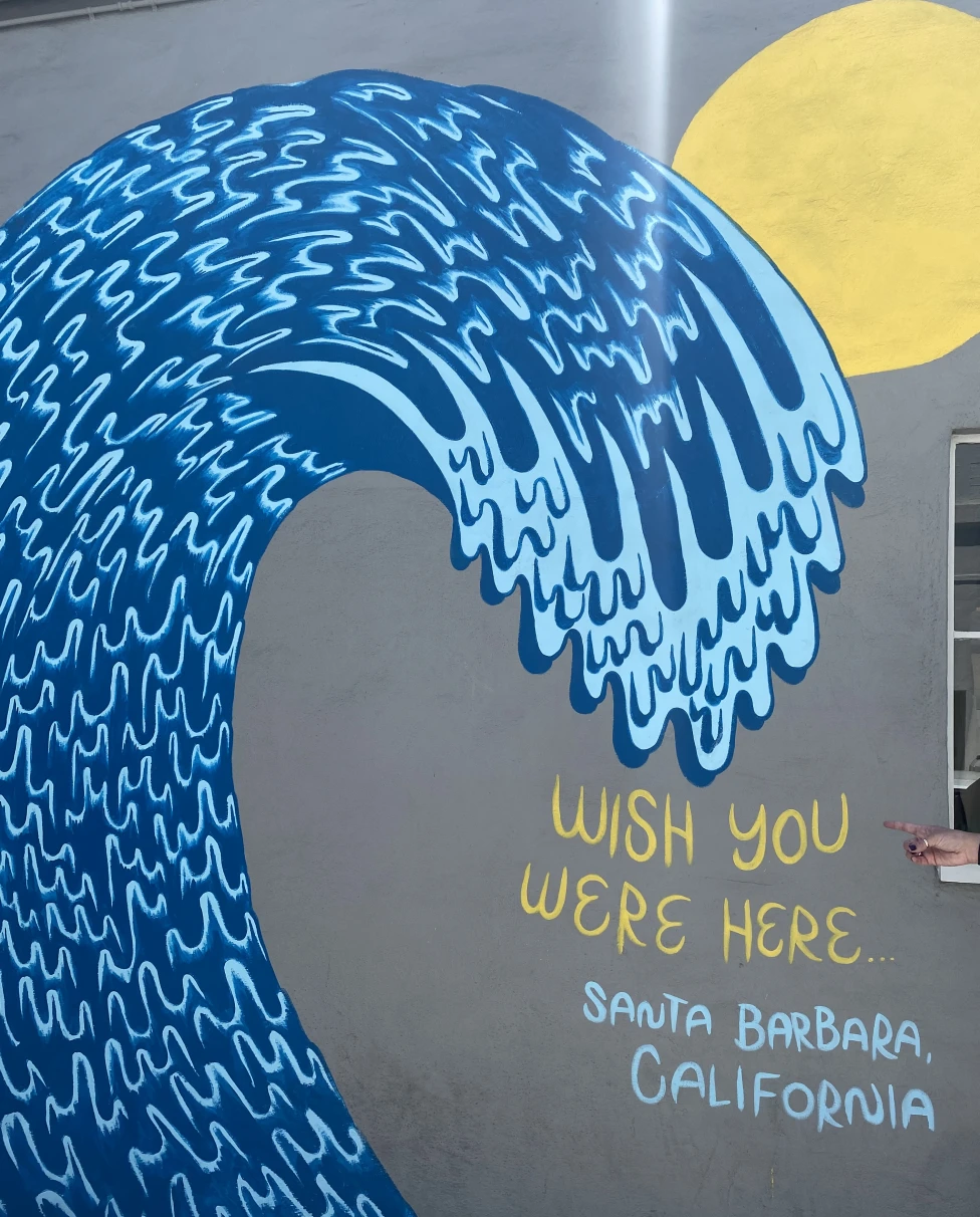 A mural of a blue wave that says "Wish you were here... Santa Barbara California" in blue and yellow lettering.