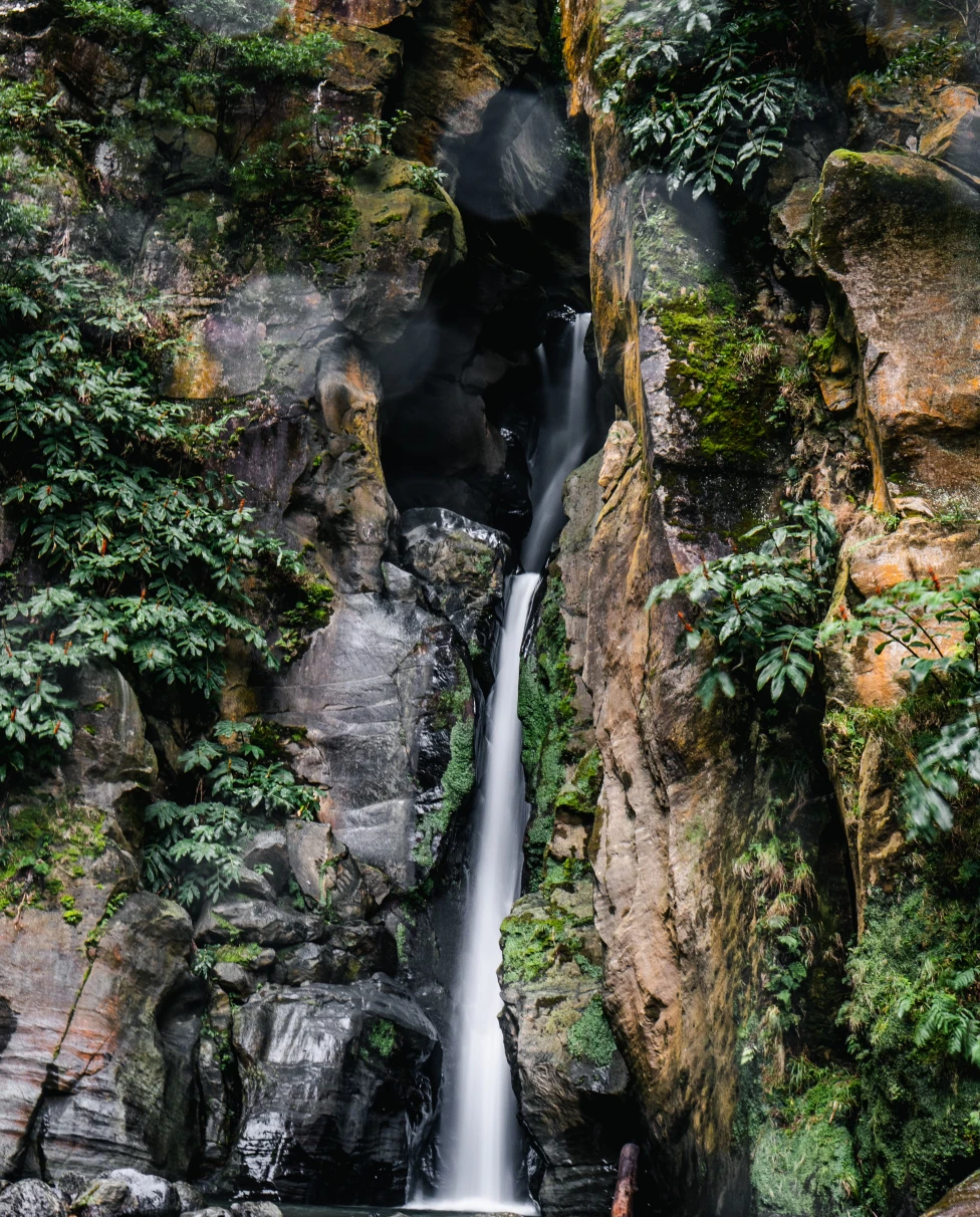 A lush green waterfall flanked by rock formations in the Azores.