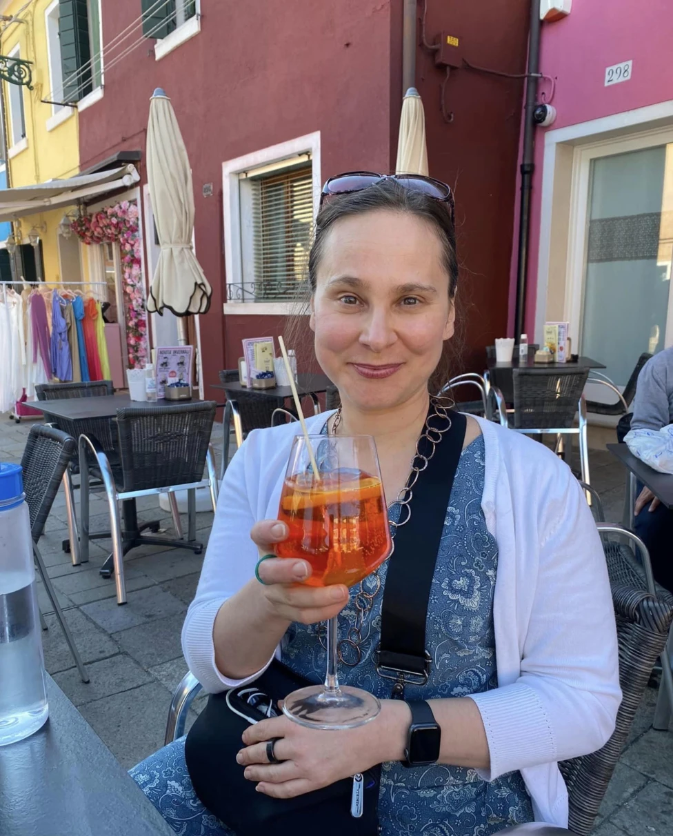 A person enjoys a refreshing orange drink at an outdoor café, with vibrant buildings and a lively atmosphere in the background.