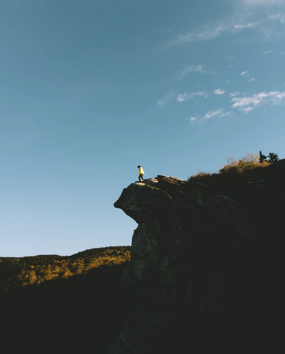 A person standing on the edge of the clifftop of Boone Mountain with blue sky overhead