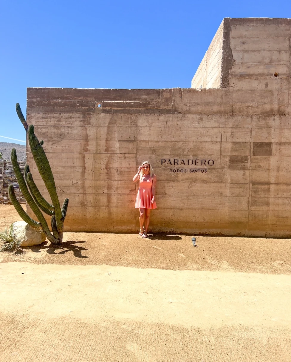 A girl standing in front of a hotel wall next to a large cactus.