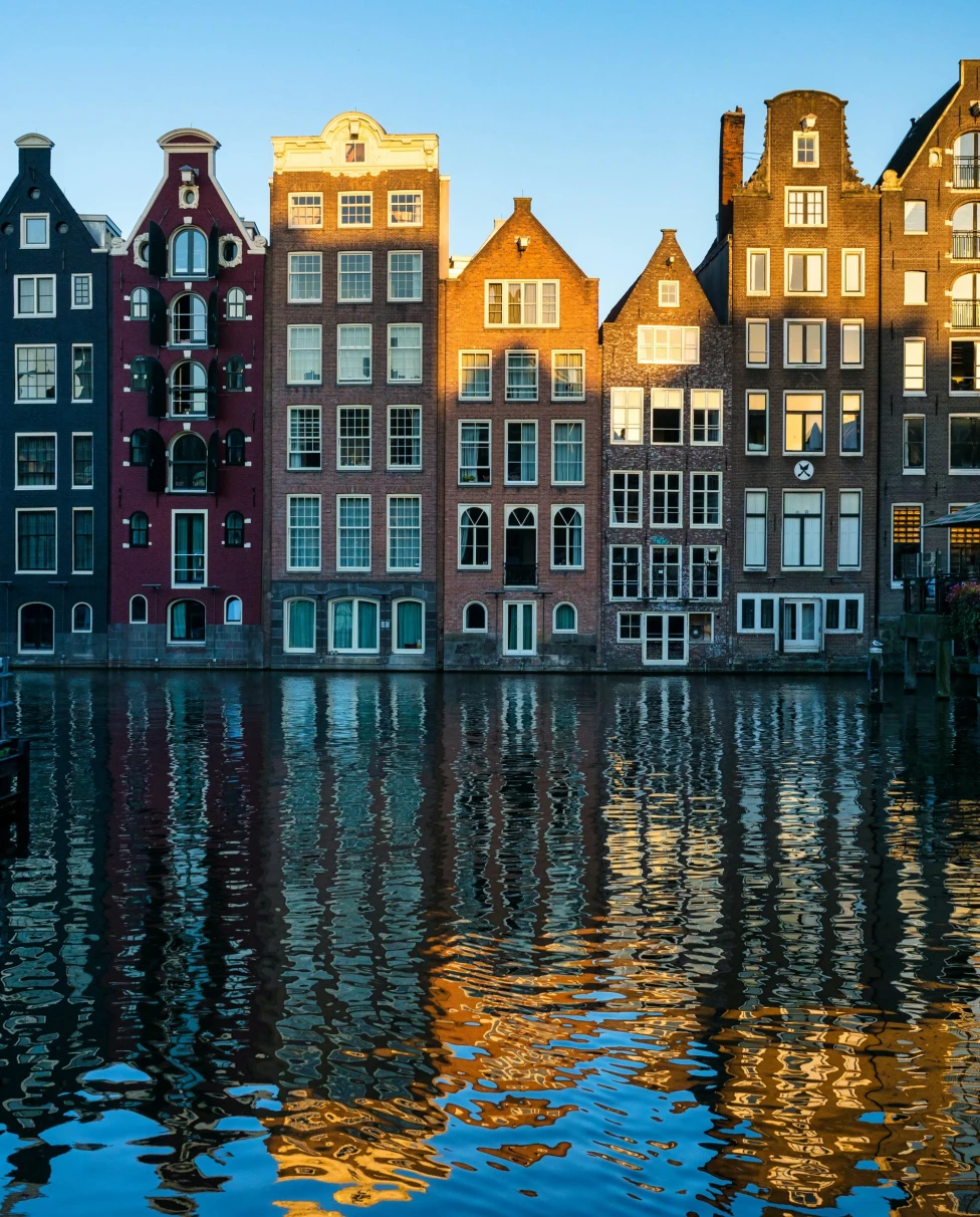 multiple story houses with big white windows on a canal reflect into the water below on a clear day