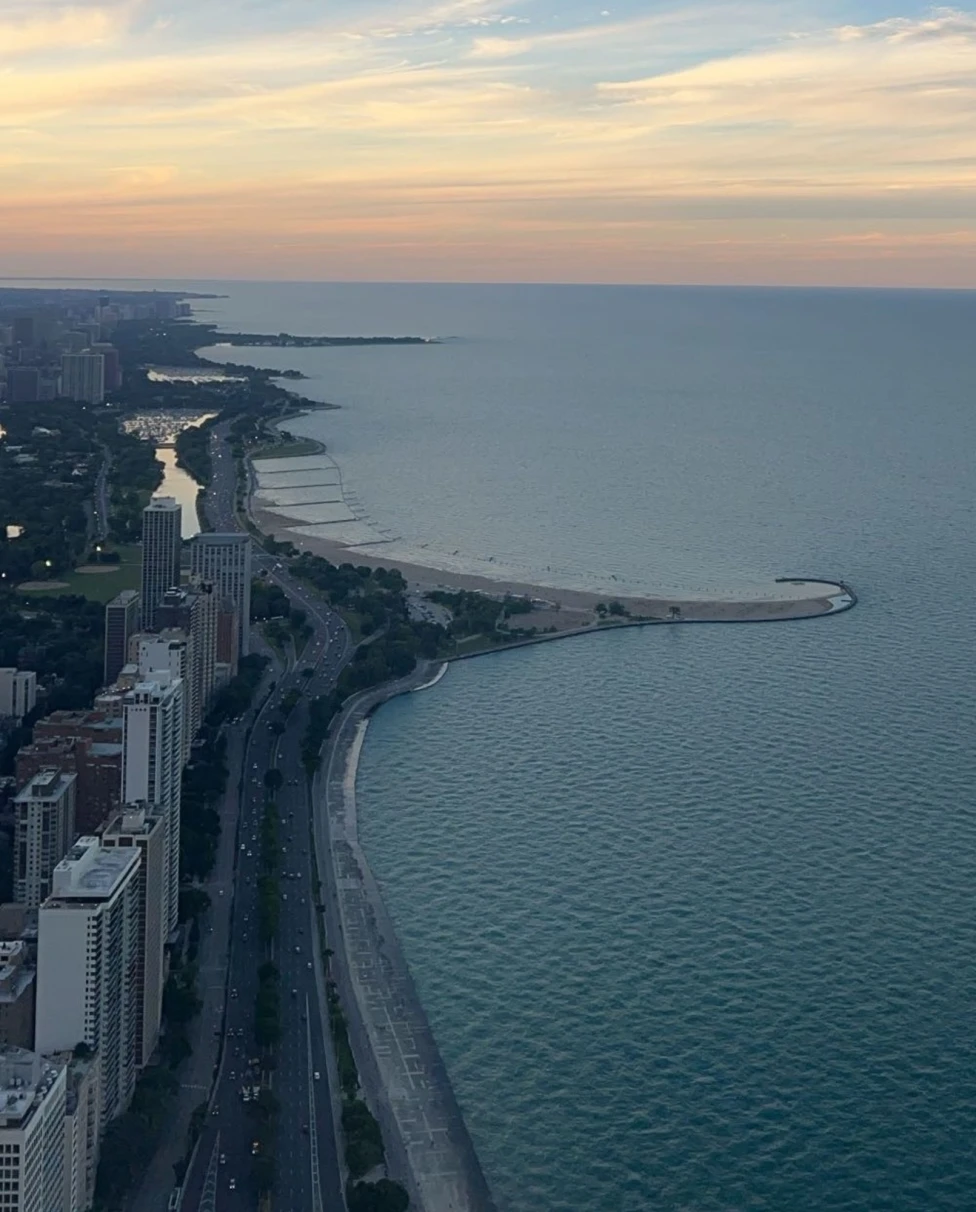 An aerial view of a coastal cityscape during twilight showcases the shoreline, buildings, and a road alongside the beach.