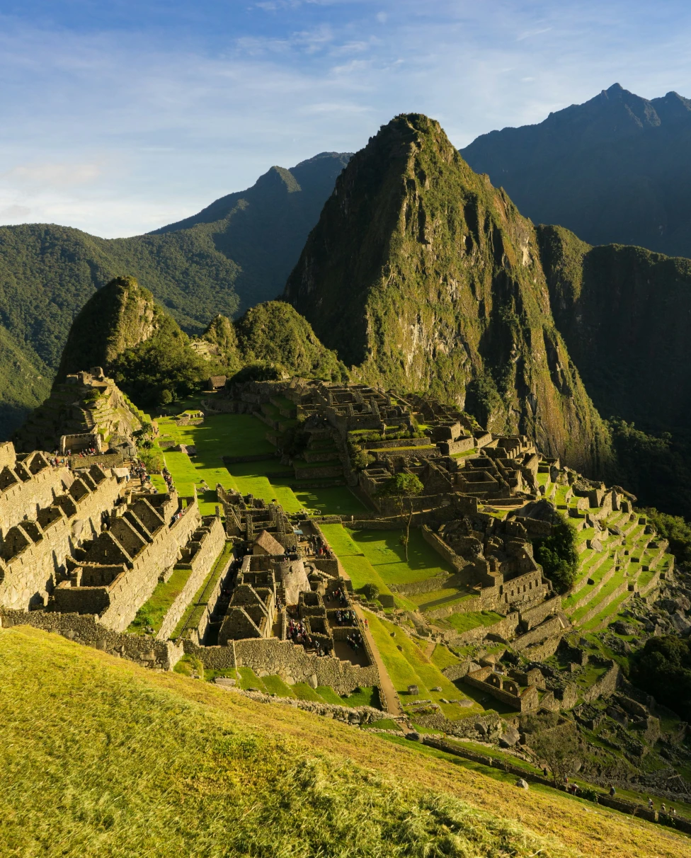 An aerial view of Machu Picchu, Peru complete with lush green grass and mountain ranges in the distance.