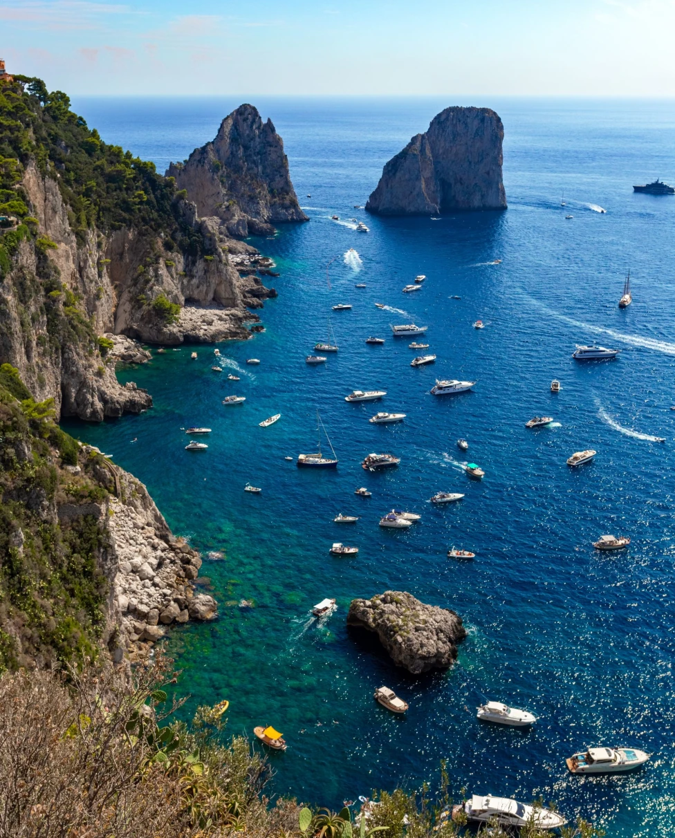 blue waters off an island with rock formations in the water and dotted with boats