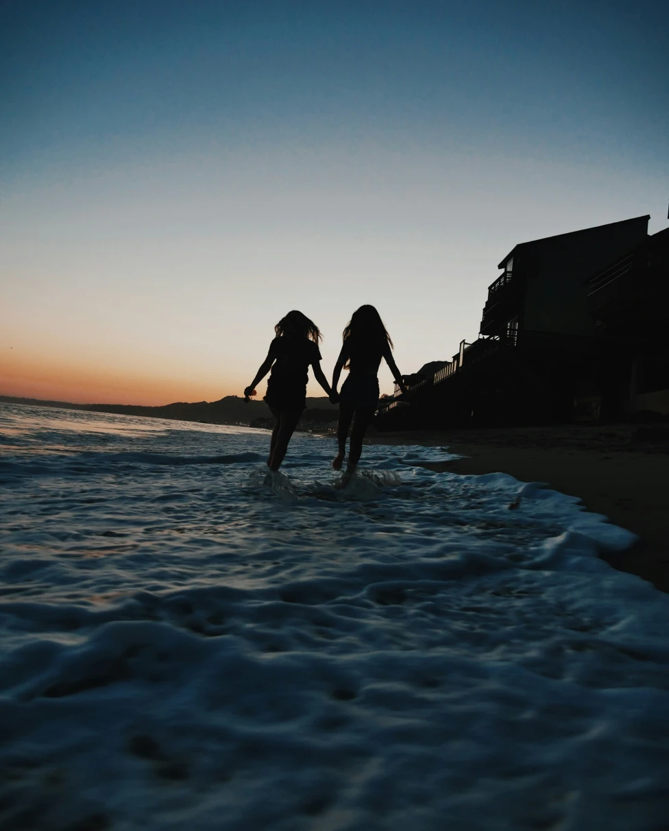 A picture of silhouette of two women running across seashore.