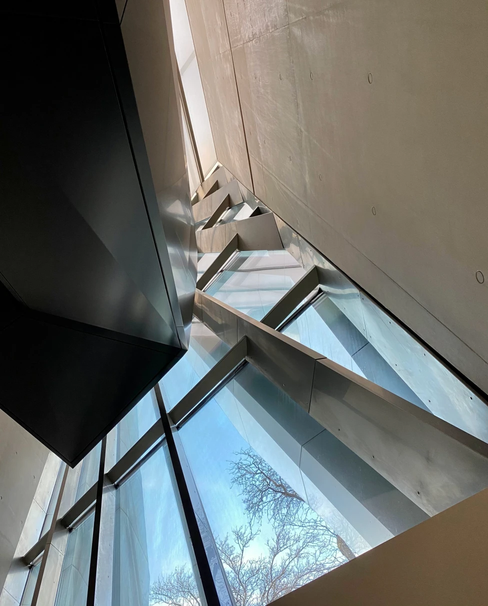 A bottom up view of a white wall and abstract window frame with silver and black beams built in angled directions.